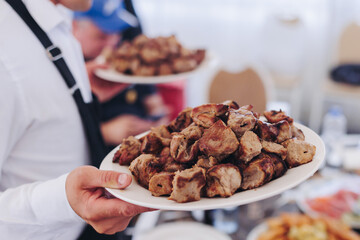 Waiter in uniform serving dishes on party event, server carrying plates with food at the table,...