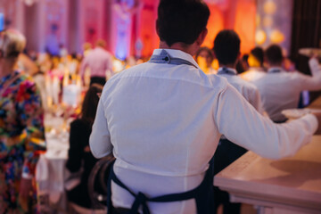 Waiter in uniform serving dishes on party event, server carrying plates with food at the table,...