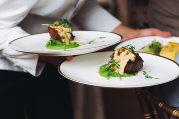 Waiter in uniform serving dishes on party event, server carrying plates with food at the table,...