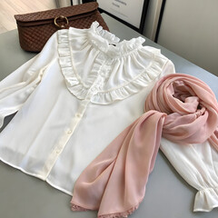 Elegant white blouse with ruffled collar and a delicate pink scarf, set against a neutral background, highlighting a classic and refined fashion ensemble ideal for style blogs or retail promotions.