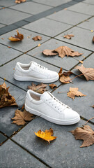 Crisp white sneakers rest on a paved surface adorned with fallen autumn leaves, capturing the essence of fall fashion and a clean, minimalist style in an outdoor setting.