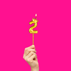 Birthday on a fuchsia background with the number 2 - Hands holding number-shaped candles