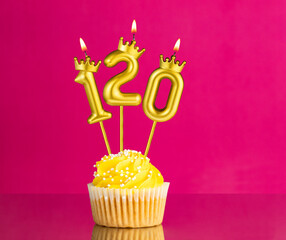 Yellow birthday cupcake with a number 120 candle - Birthday card on a pink background