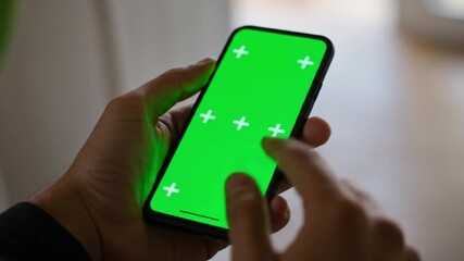 Person holding smartphone with green screen and white tracking markers using their fingers to interact with it