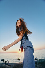 lifestyle woman in modern boho-western denim street style with loose hair at sunset by the sea,...