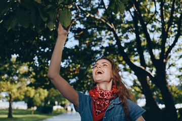 lifestyle woman in modern boho-western denim street style joyfully reaching for fruit on tree in...