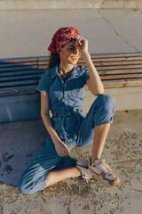 Lifestyle woman in modern boho-western denim street style wearing a red bandana, sitting outdoors...