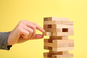 Lviv, Ukraine - December 04, 2023: Woman playing Jenga tower on yellow background, closeup