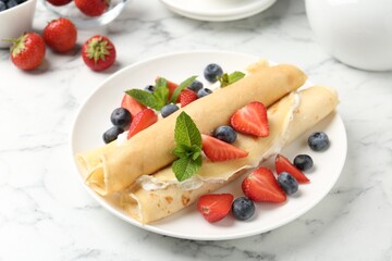 Tasty crepes with cream, berries and mint on white marble table, closeup