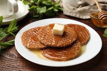 Tasty Dutch waffles (stroopwafels) with honey and butter cube on wooden table, closeup