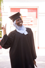 Portrait of happy african woman wearing hijab and graduation gown. 