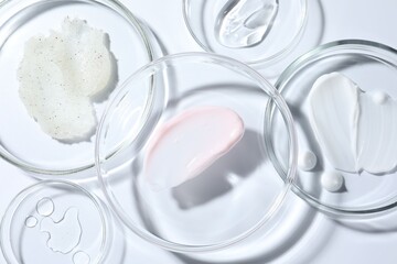 Different cosmetic products in Petri dishes on white background, closeup