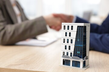 Real estate agent and client shaking hands at desk in office, focus on house model