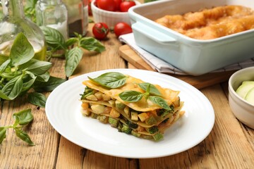 Piece of tasty vegetarian lasagna and ingredients on wooden table
