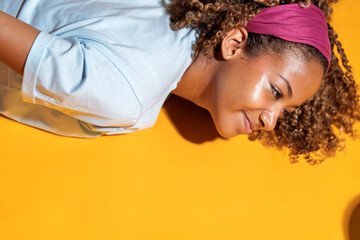 Young black woman lying down and smiling on yellow background