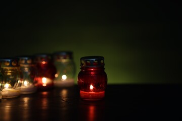 Many grave candles on black table against green background, closeup