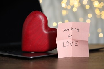 Online dating site. Sticky note with text Searching For Love, decorative heart and laptop on wooden...
