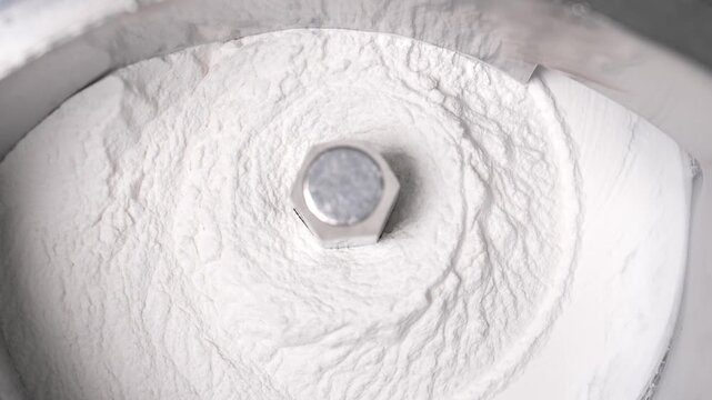Close-up of a stainless steel pharmaceutical machine mixing white powder raw material for medicine or vitamin production in a cleanroom environment.
