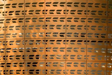 Close-up of a copper-colored facade with a repeating pattern of stylized arrow-shaped perforations,...