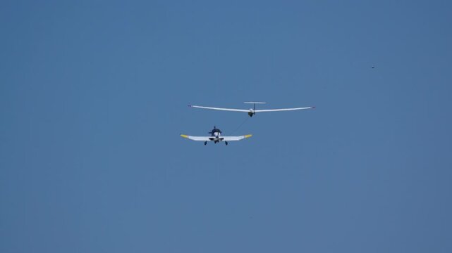 Small plane tows a white glider through a clear blue sky, preparing for flight on a sunny day