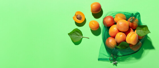 Eco bag with fresh apricots and leaves on green background