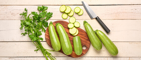 Board with many fresh green zucchini and parsley on white wooden background