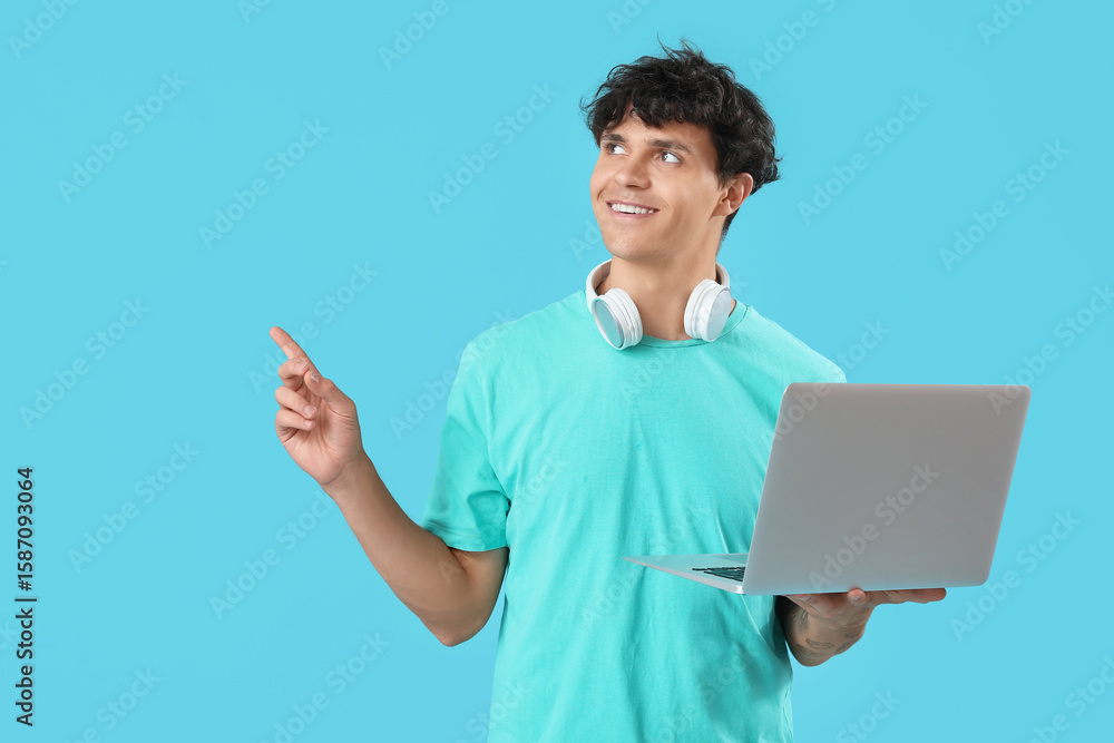 Poster male programmer with laptop pointing at something on blue background