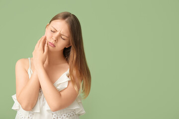 Young woman suffering from toothache on green background