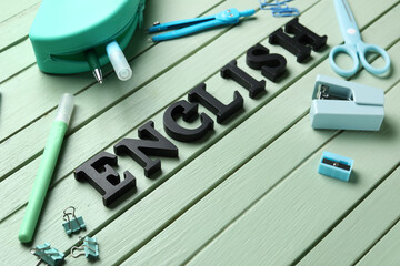 Stationery and word ENGLISH on green wooden background