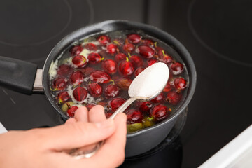 Woman preparing tasty gooseberry jam on electric stove