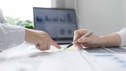 Two people reviewing financial reports and charts on a desk with a laptop
