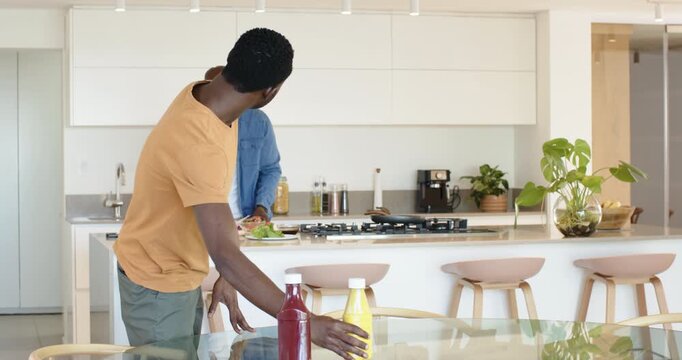 African American father and son grabbing ketchup  and  mustard in kitchen squeezing ketchup on burge