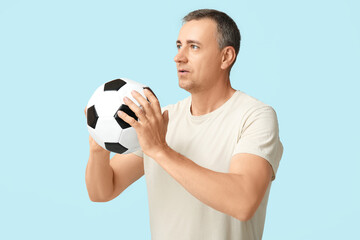 Handsome mature man playing with soccer ball on blue background