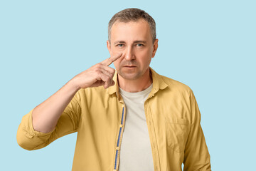Ill mature man pointing at nose on blue background