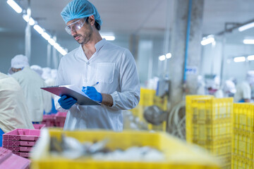 A supervisor in a food processing plant wearing protective gear, inspecting a fish while holding a clipboard, emphasizing quality control, hygiene, and safety in the seafood production process.
