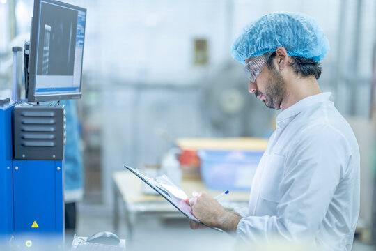 A supervisor in protective gear reviewing data on a computer screen at a food processing facility, holding a clipboard, emphasizing technology, quality control, and efficiency in industrial.
