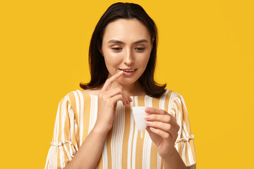Beautiful young woman with menstrual cup on yellow background