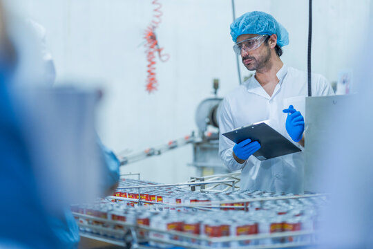 A food processing supervisor wearing protective gear and holding a clipboard, inspecting machinery on a production line, emphasizing quality control, safety, and efficiency in industrial operations.