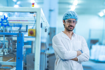 A confident food processing supervisor in protective gear, standing with arms crossed next to...
