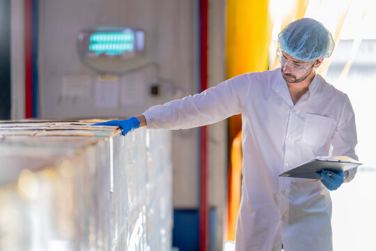 A meticulous male scientist in a sterile environment meticulously documents quality control data on a clipboard in a pharmaceutical production facility.