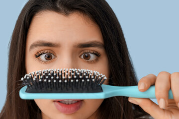 Stressed young woman with hair loss problem and brush on blue background, closeup