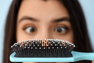 Stressed young woman with hair loss problem and brush on blue background, closeup