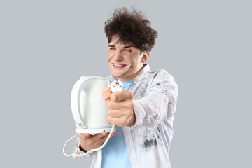 Electrocuted young man with burnt face and electric kettle on light background