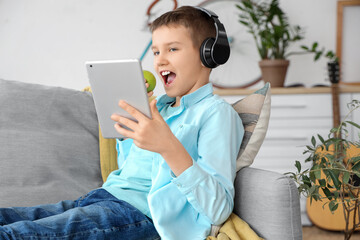 Teenage boy in headphones eating apple and using tablet on sofa in living room