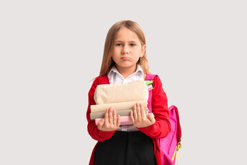Upset little schoolgirl with backpack, pencil case and books on white background