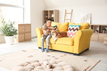 Little happy Asian boy with cute Corgi dog and teddy bear sitting on sofa at home
