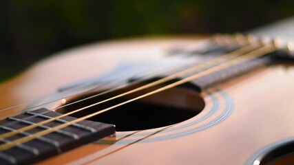 Close up shot of an acoustic guitar focusing on the strings and fretboard with blurred background