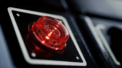 Close up of a red illuminated button on a black panel with a square frame around the button