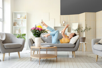 Young woman with mobile phone lying on sofa and roses in vase at home