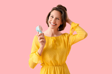 Young woman with portable electric fan on pink background
